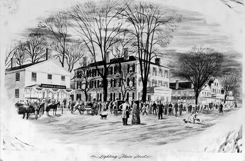 Black-and-white engraving captioned 'Lighting Main Street' depicting a busy small-town street with horse carriages, pedestrians, and storefronts under bare trees.